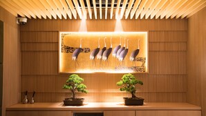 A reception area with a wooden slatted wall, a framed artwork of birds, and two potted bonsai trees. - The Centurion Hotel Classic Akasaka (Tokyo)