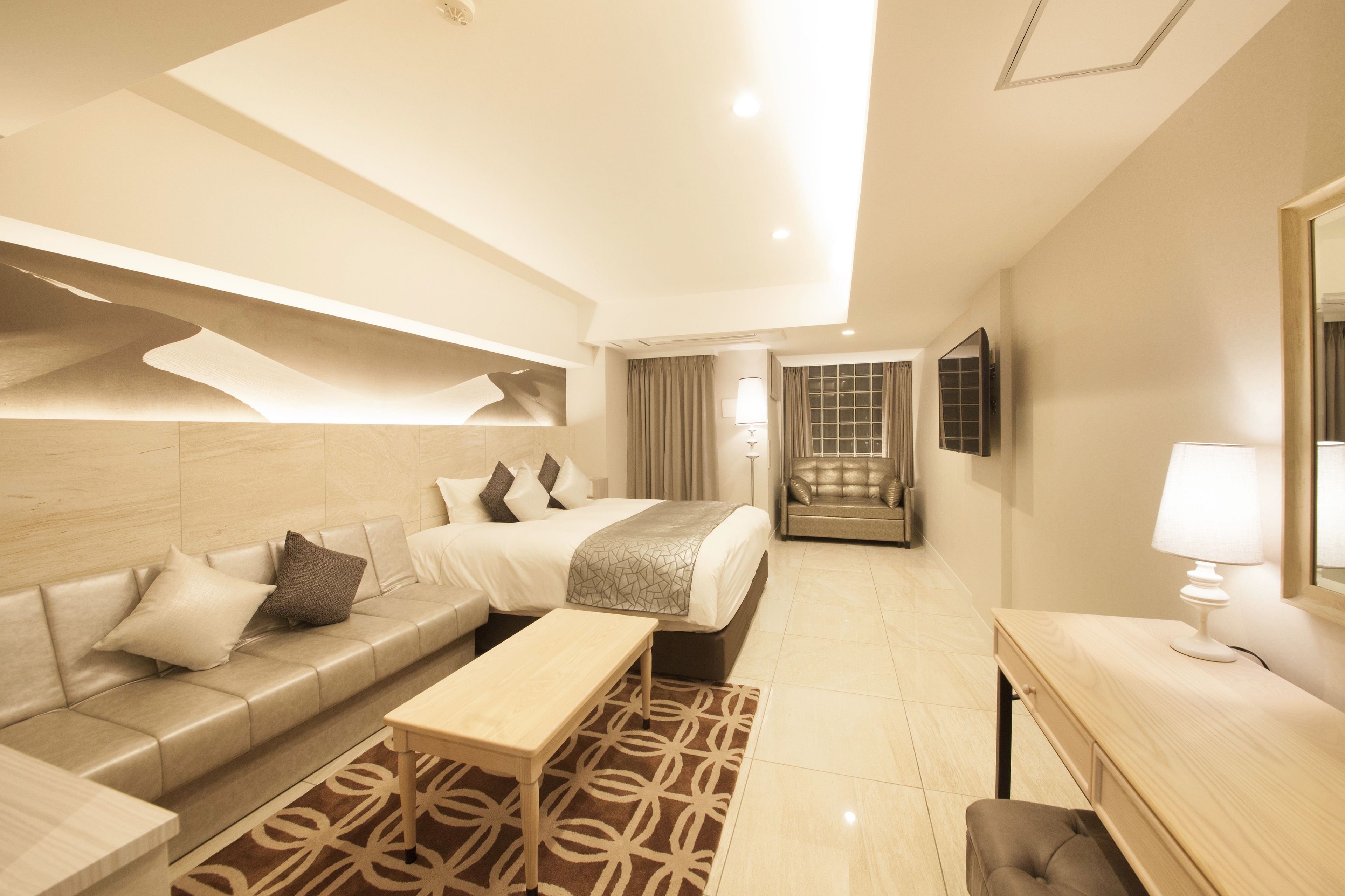 A modern hotel room with a sofa, a bed, a desk, and a mirror.