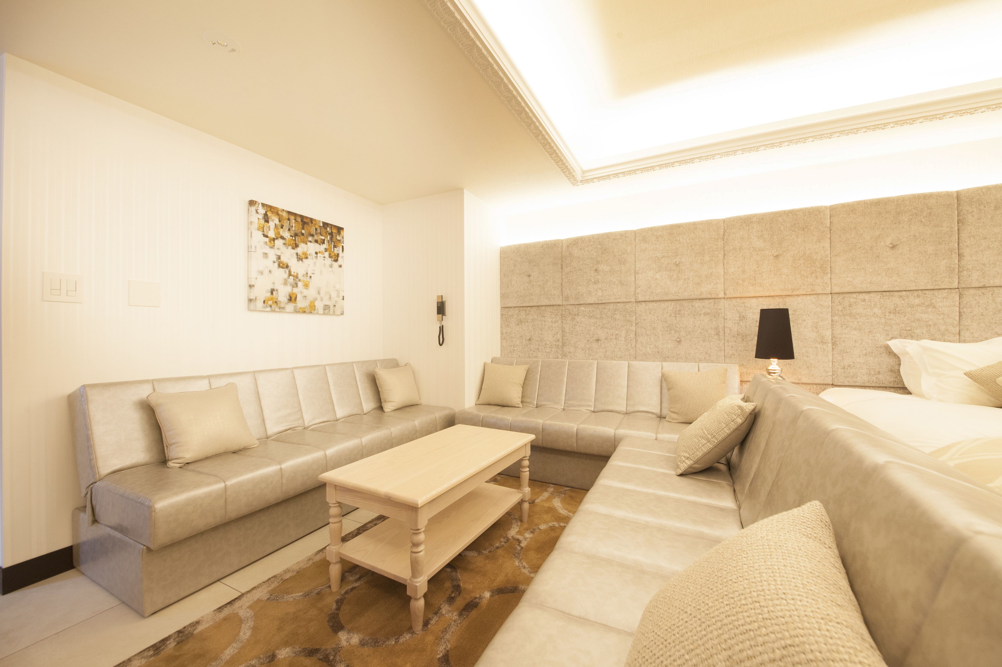A modern hotel room with a sectional sofa, a small wooden table, and a large bed.
