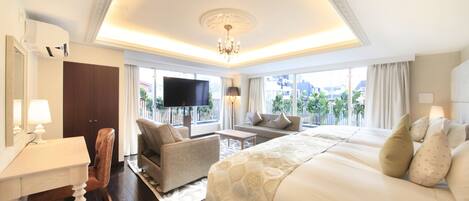 A spacious hotel room with a large bed, a sofa, a desk, and a TV.