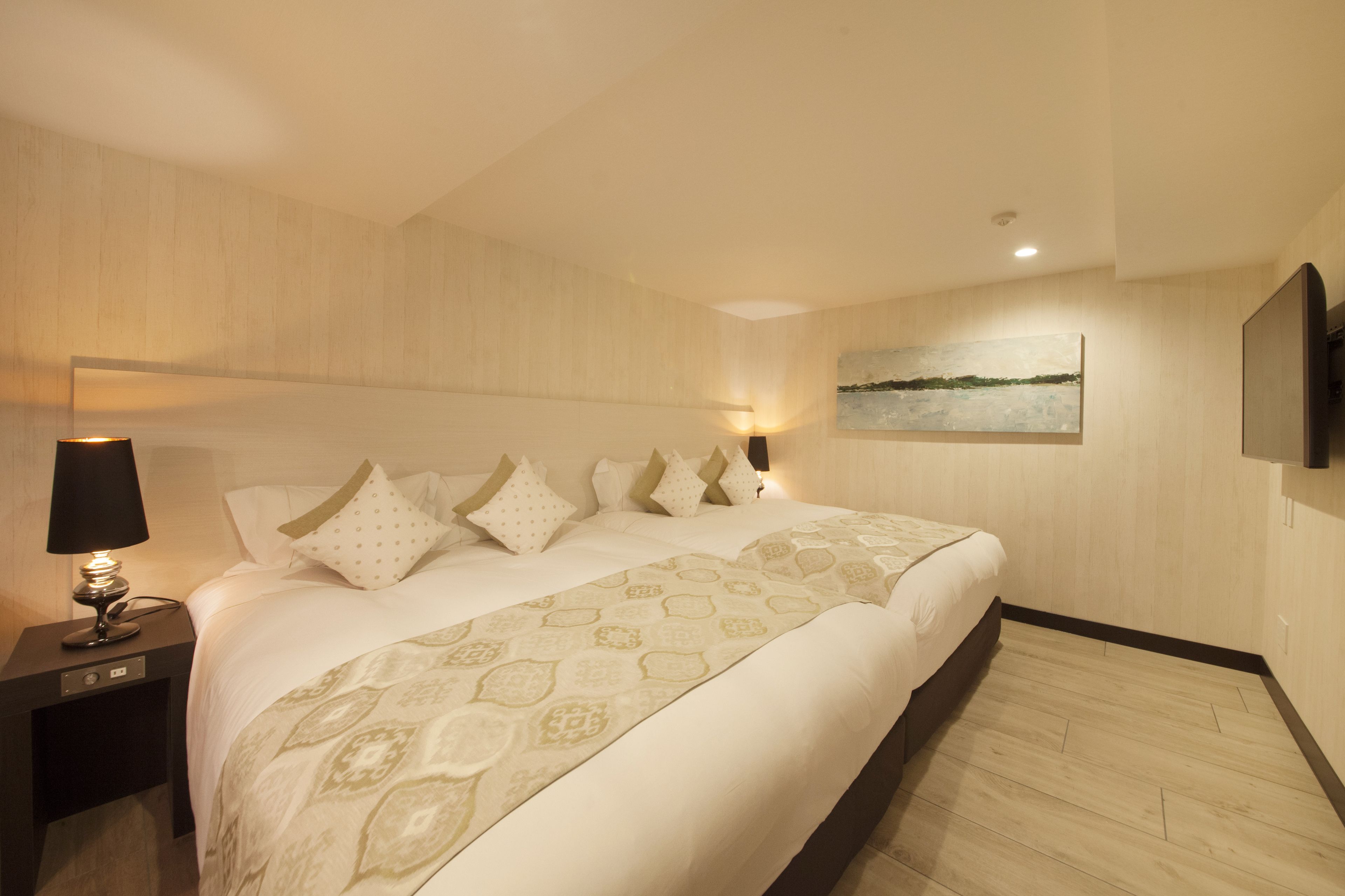 Une chambre d’hôtel moderne avec un grand lit, une table de chevet avec une lampe et un tableau au mur.