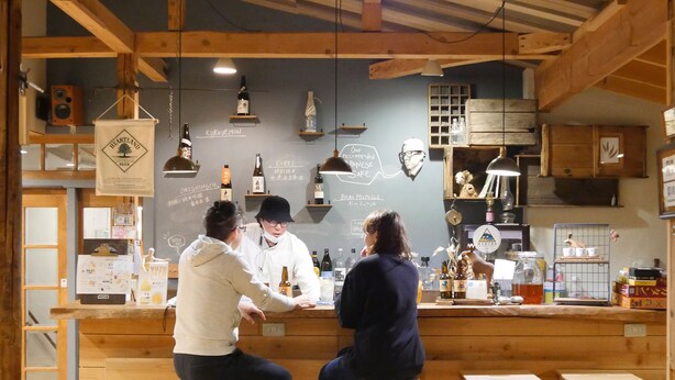 Um bar com vigas de madeira, um menu em lousa e diversos copos e garrafas no balcão.