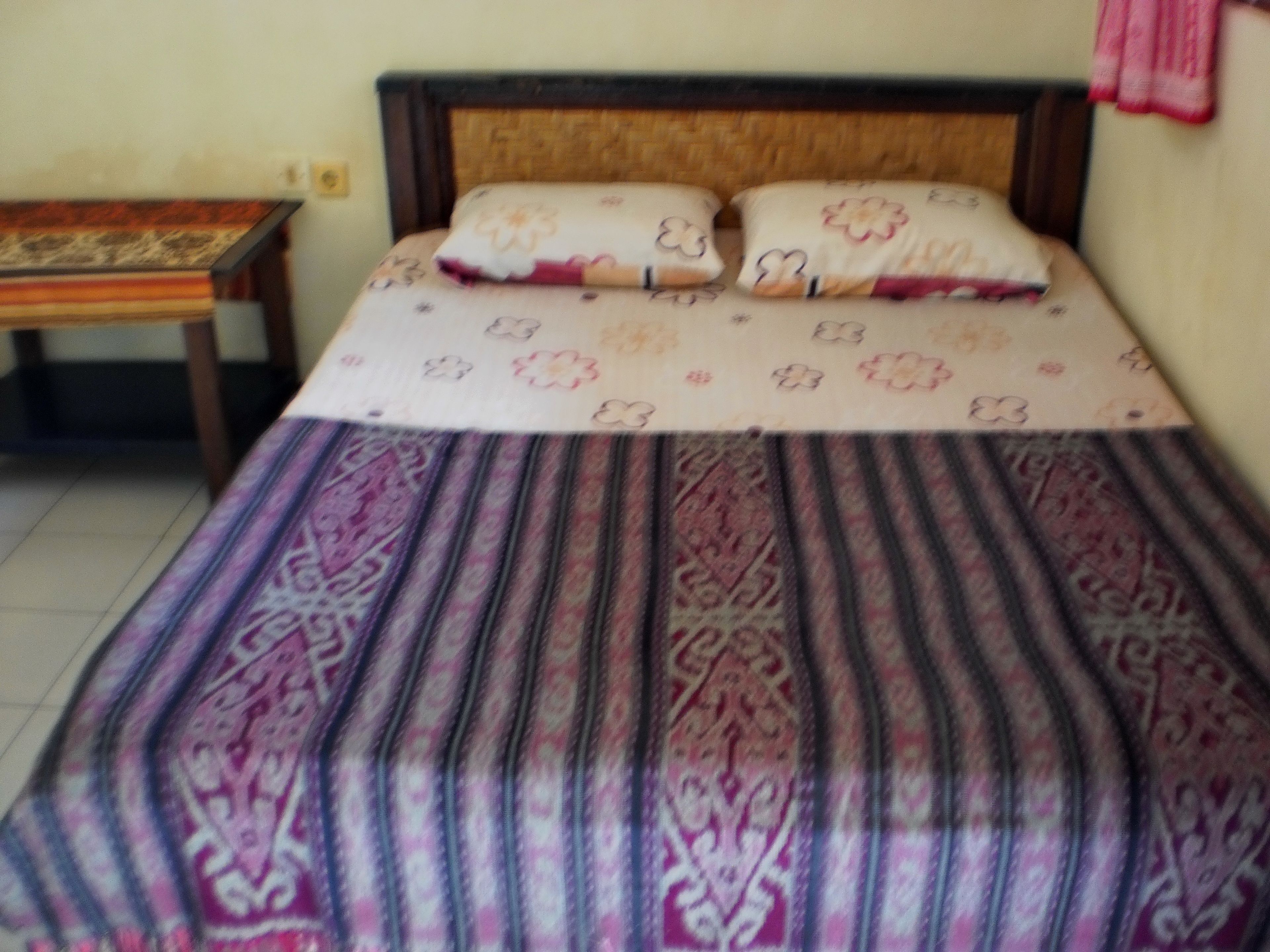 A bed with a patterned bedspread and pillows, a wooden headboard, and a small table beside the bed.