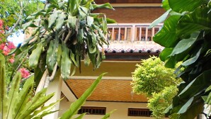 A traditional building with a tiled roof, wooden balconies, and a window with a bamboo grill design. - Arjuna Homestay Ubud (Ubud)