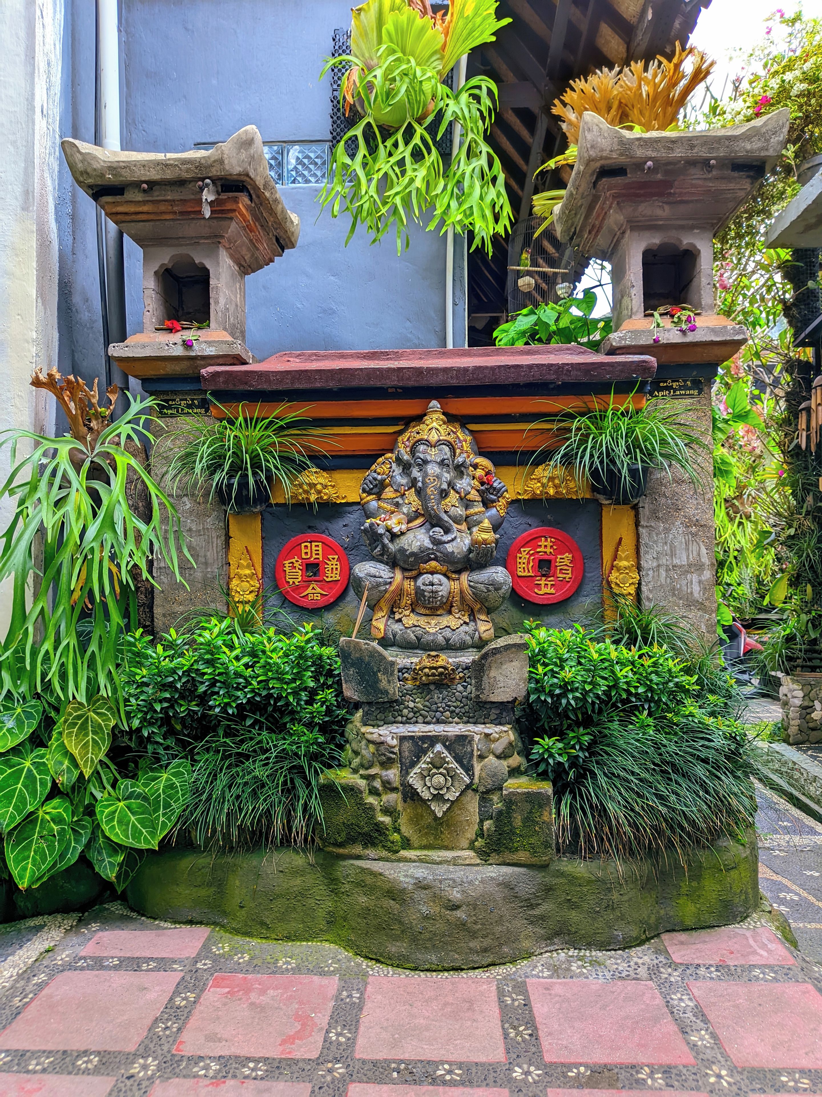 A stone structure with a central statue, surrounded by greenery and red circular decorations.