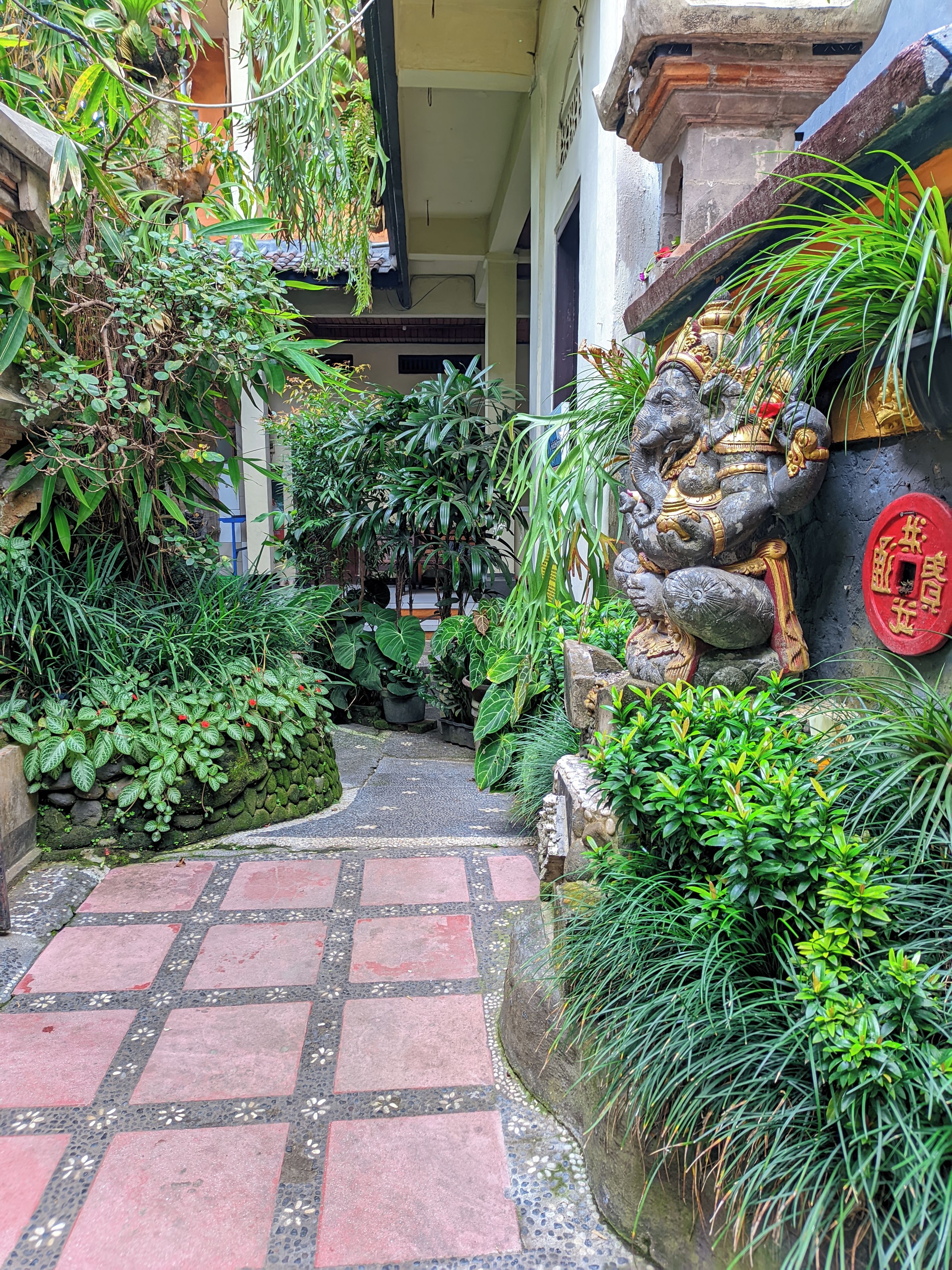 A pathway leading to a building entrance surrounded by lush greenery and a decorative stone statue.