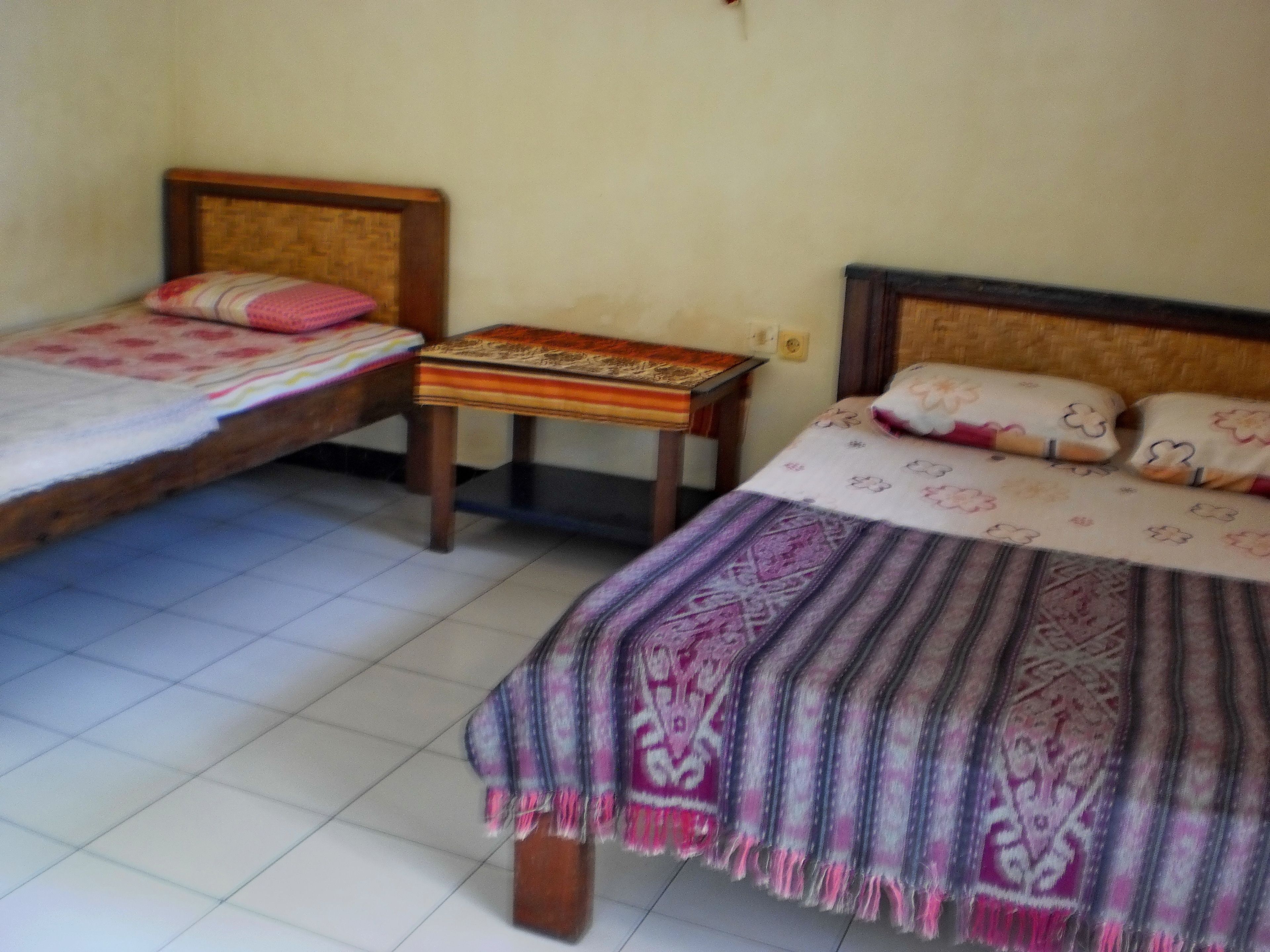 A room with two single beds, each with a wooden headboard and a patterned bedspread. There is a small wooden table between the beds.