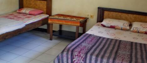A room with two single beds, each with a wooden headboard and a patterned bedspread. There is a small wooden table between the beds.