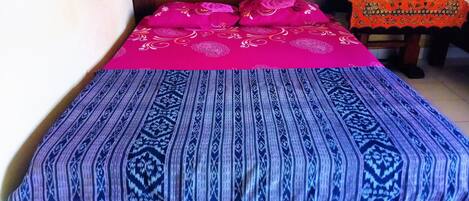 A bed with a patterned bedspread and pillows, a wooden headboard, and a small table with a patterned tablecloth.