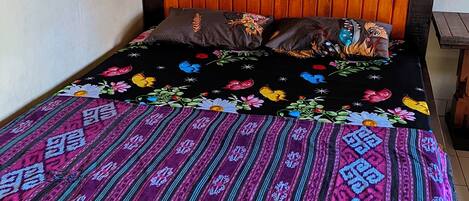 Una cama con una colcha estampada y almohadas, cabecero de madera y suelo de baldosas.