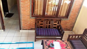 A room with a wooden bench, a table with a patterned tablecloth, and a window with curtains. - Arjuna Homestay Ubud (Ubud)