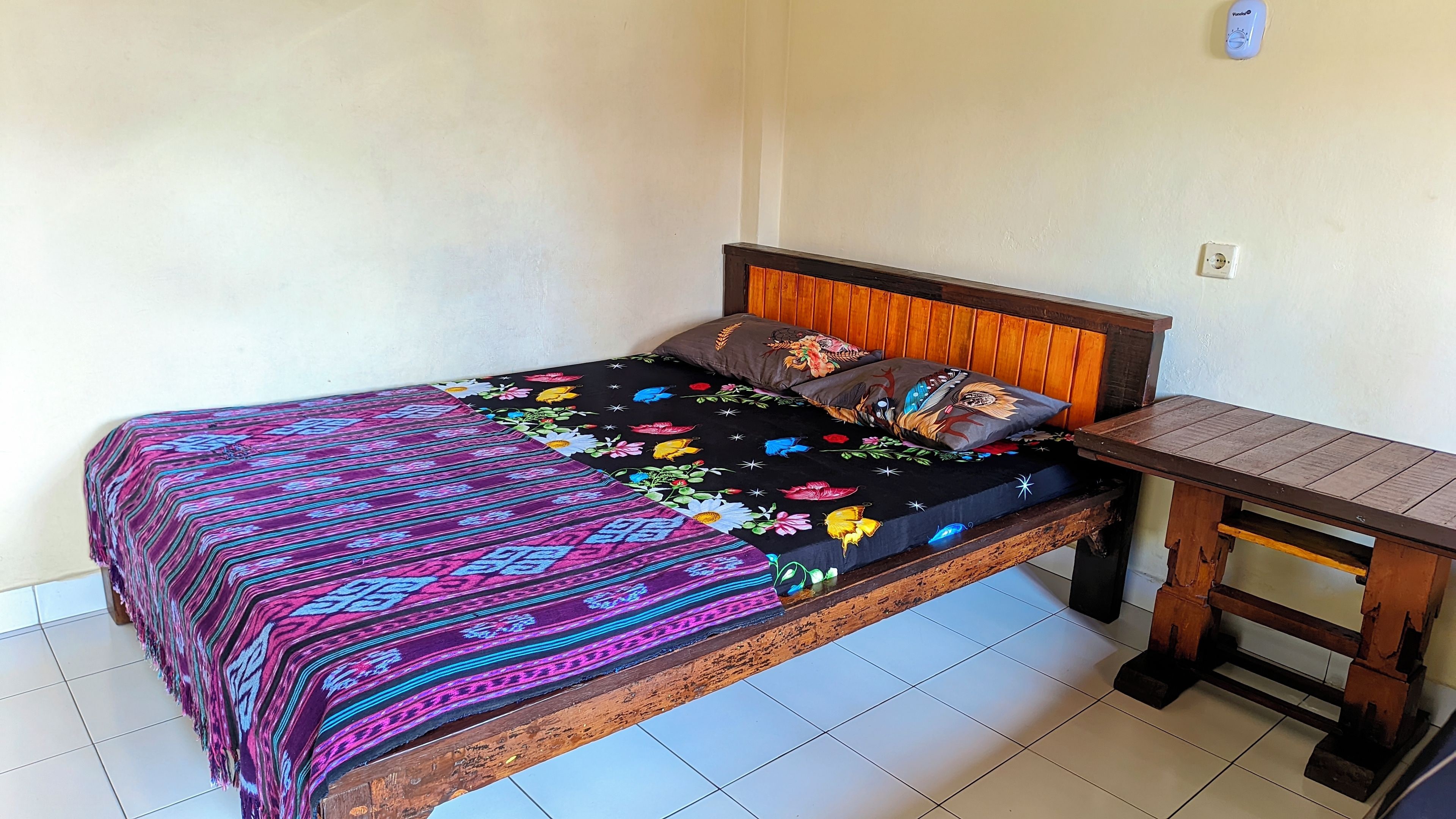 A bed with a colorful bedspread and pillows, a wooden headboard, and a nightstand with a lamp.