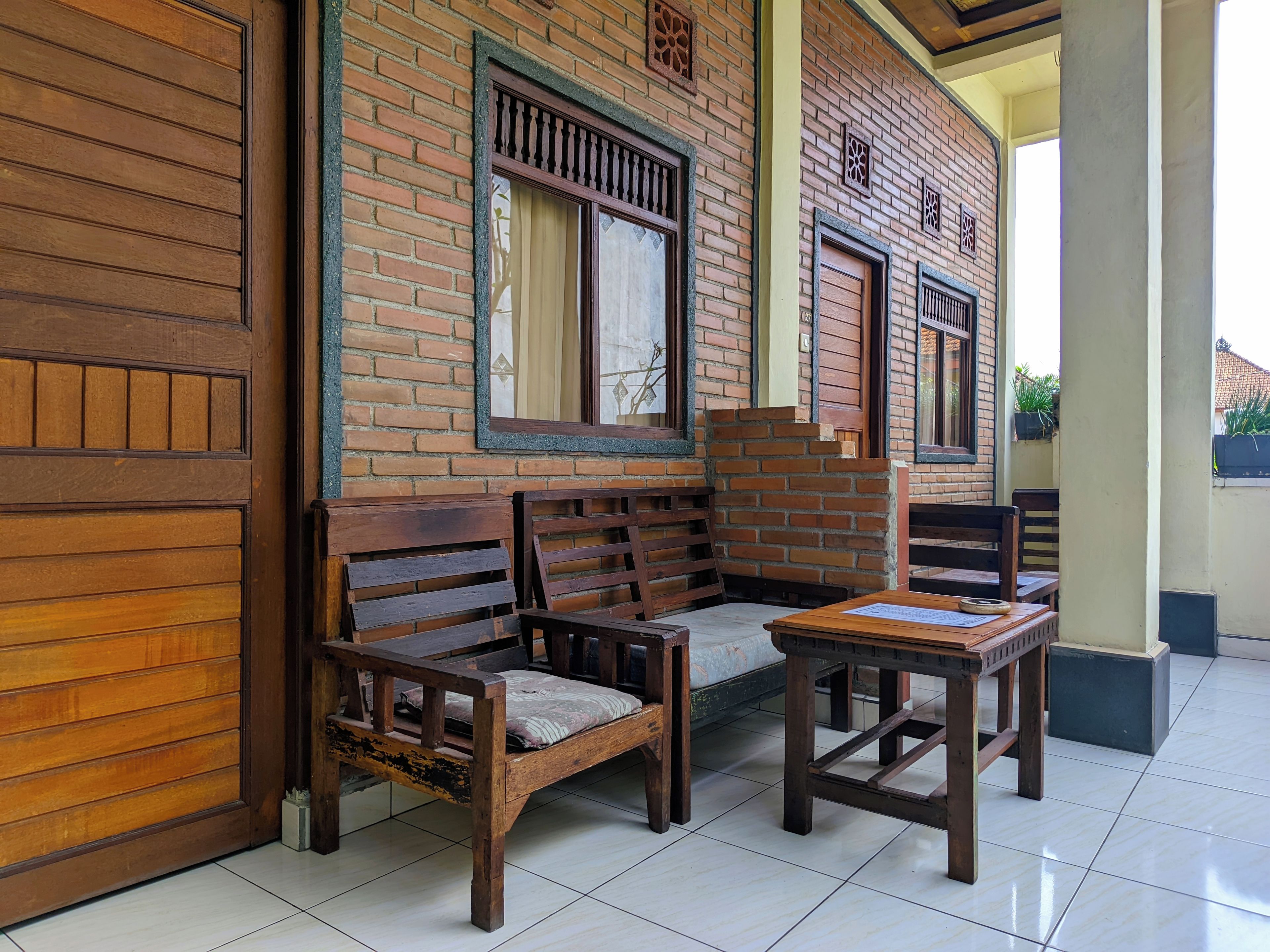 Un conjunto de banco y mesa de madera frente a un muro de ladrillo con ventanas y una puerta.