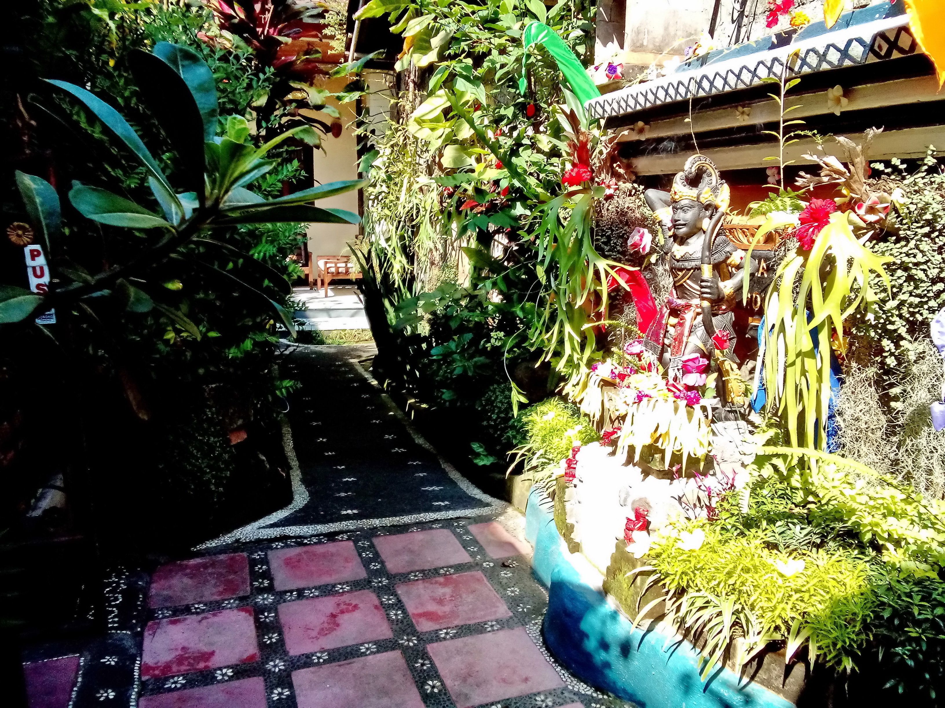A narrow pathway with patterned tiles leading to a decorated area with plants and statues.
