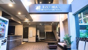 Een receptiegedeelte met een bord voor Livemax Hotels & Resorts, een automaat, een receptiebalie en een trap die naar een verdieping leidt.