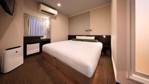 Una habitación de hotel con una cama grande, un escritorio con lámpara, un refrigerador pequeño y un equipo de aire acondicionado.