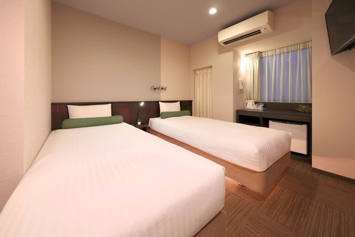 A hotel room with two beds, a desk with a chair, a flat-screen TV, and an air conditioning unit.