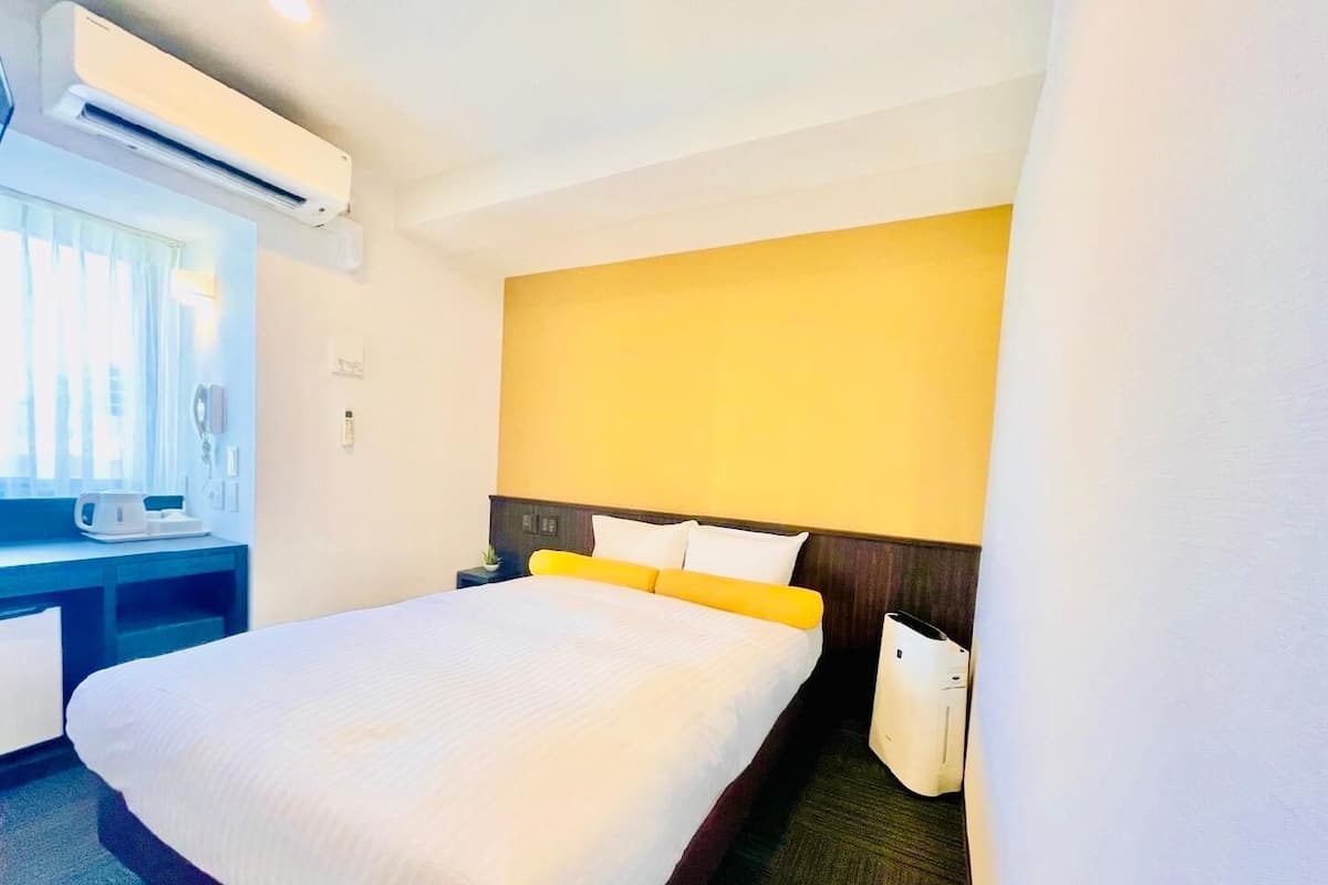 A hotel room with a bed, a desk, an air conditioning unit, and a window.