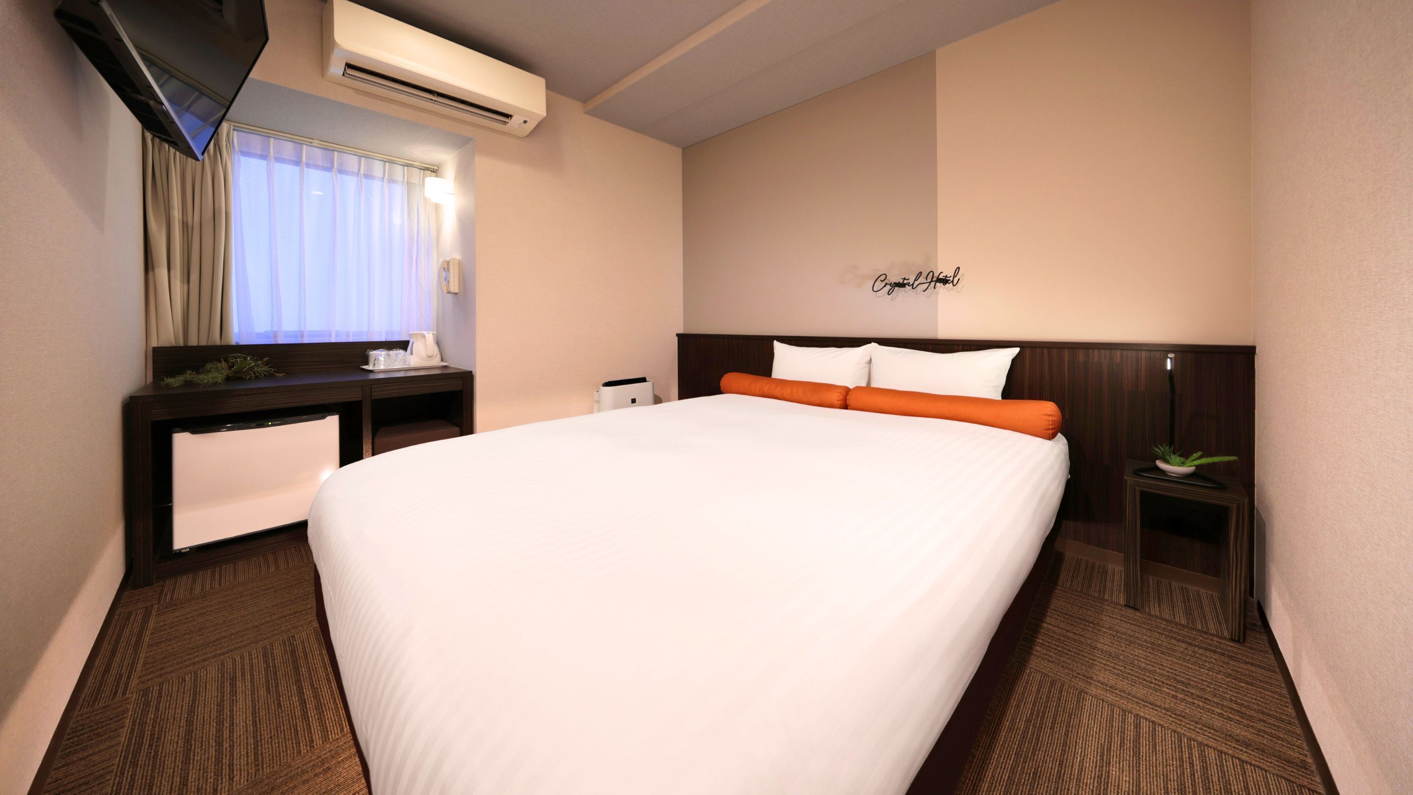 Habitación de hotel con una cama grande, un escritorio con silla, un televisor y aire acondicionado instalado en la pared.