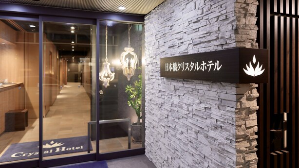Entrada de hotel con un muro de piedra y un letrero que indica un hotel de estilo japonés.