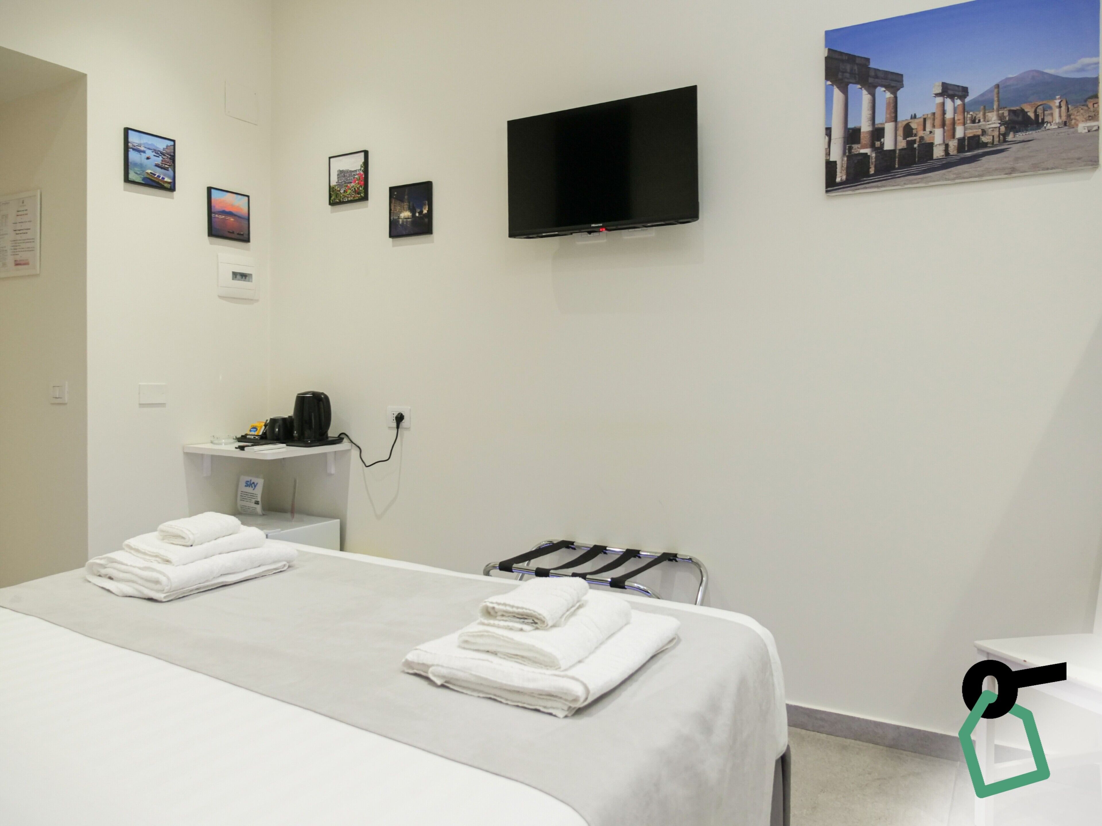 A hotel room with a bed, a TV mounted on the wall, and a small table with a kettle.
