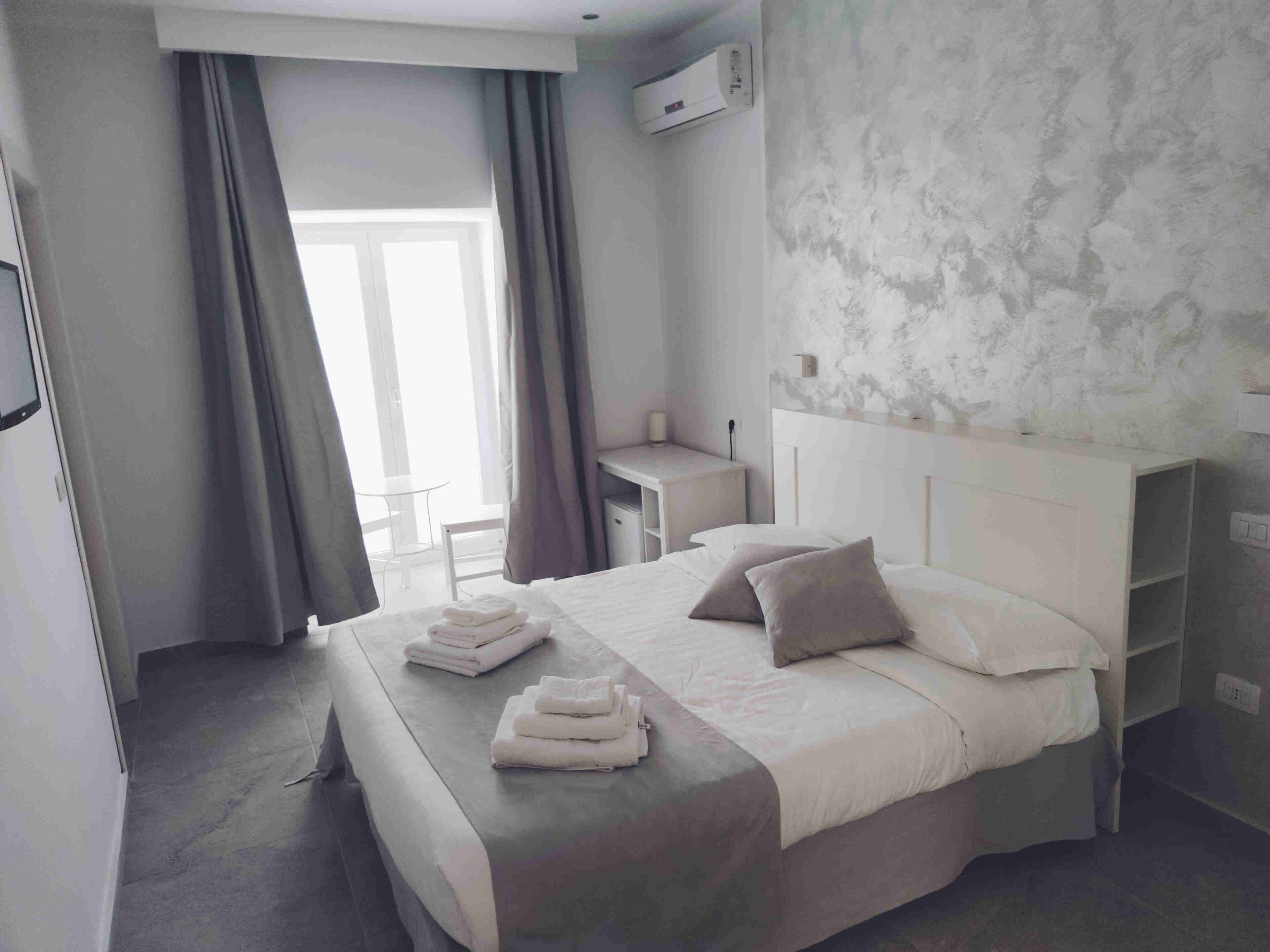 A hotel room with a bed, a desk, a chair, and a window with curtains.