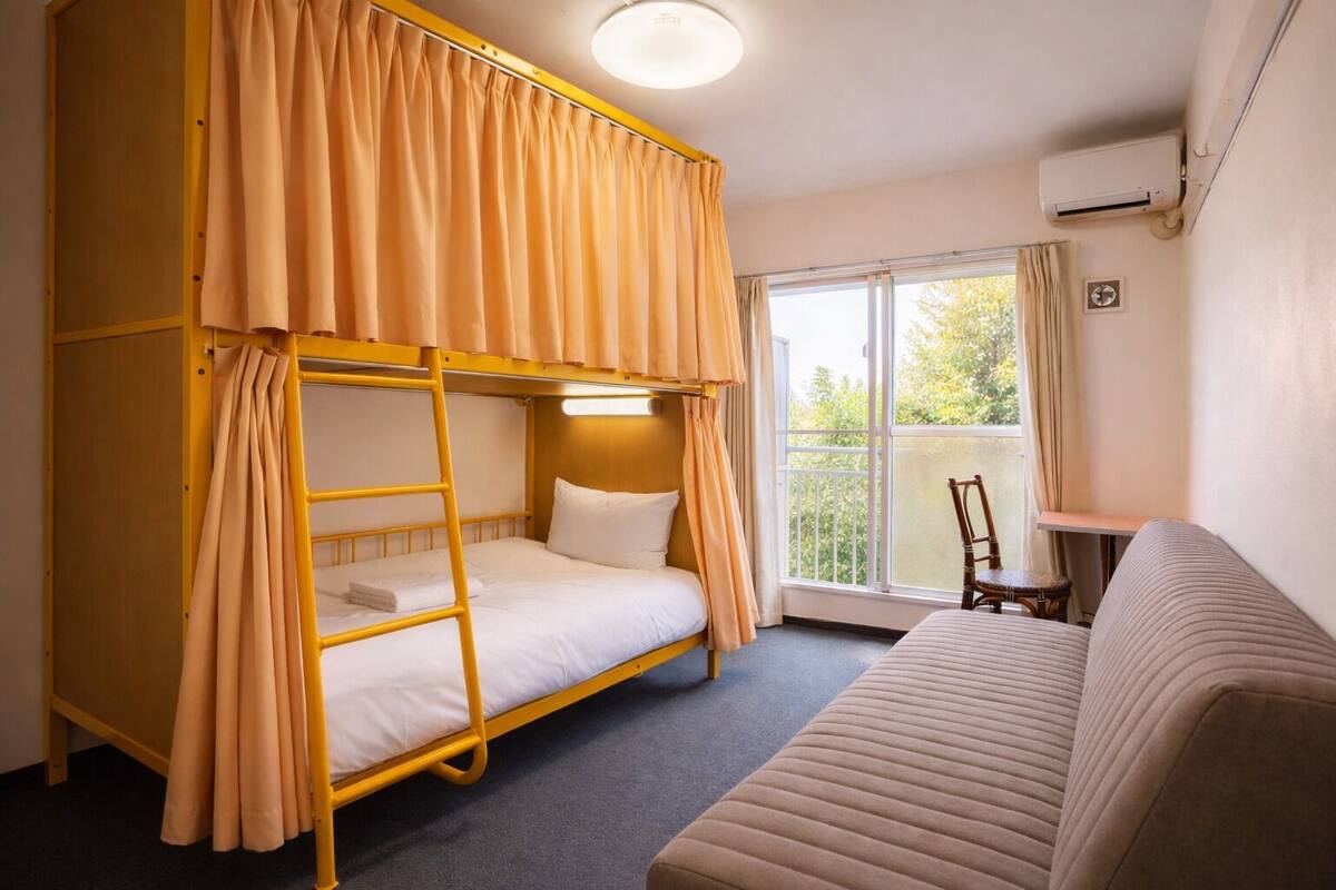 A room with a bunk bed, a sofa, a small table, and a window with curtains.