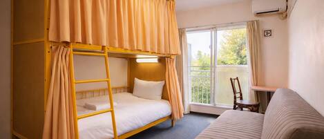 A room with a bunk bed, a sofa, a small table, and a window with curtains.