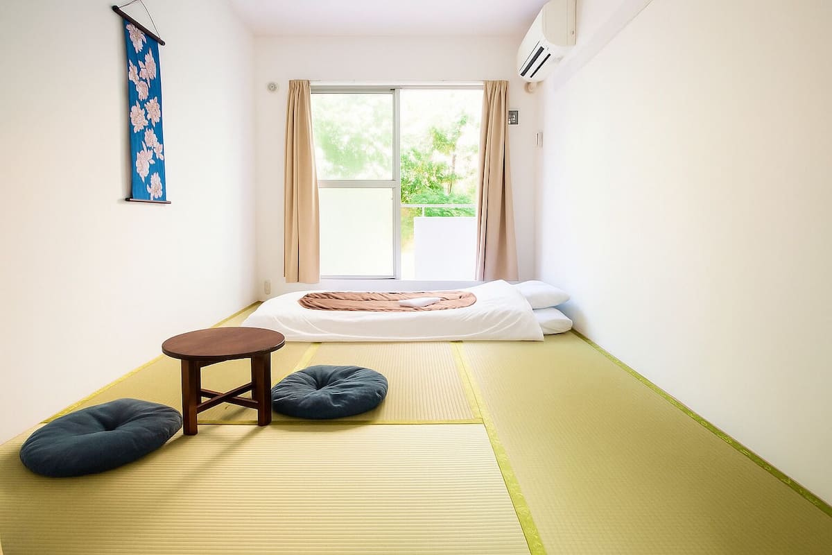 A room with a bed, a small table, and two cushions on tatami mats.