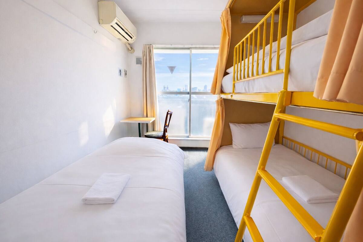 A hotel room with two beds, a window with a city view, an air conditioning unit, and a chair.