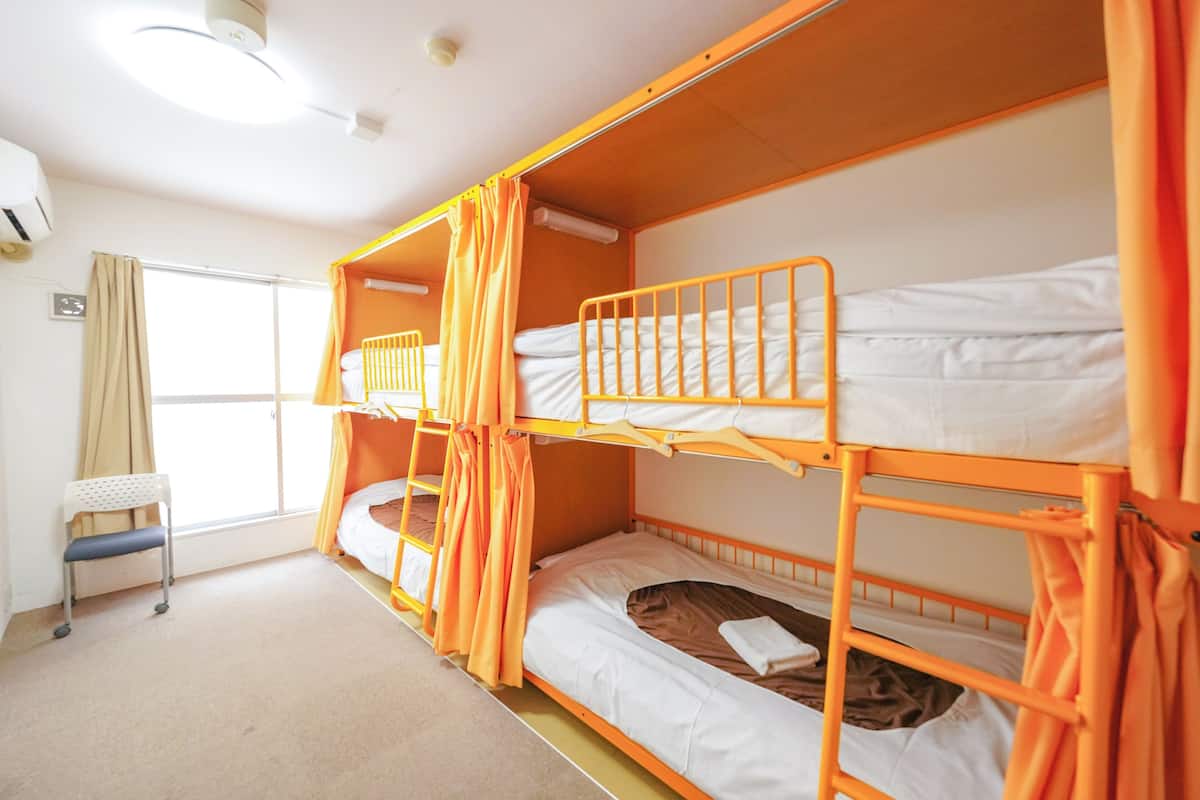 A room with bunk beds, a chair, and a window with curtains.