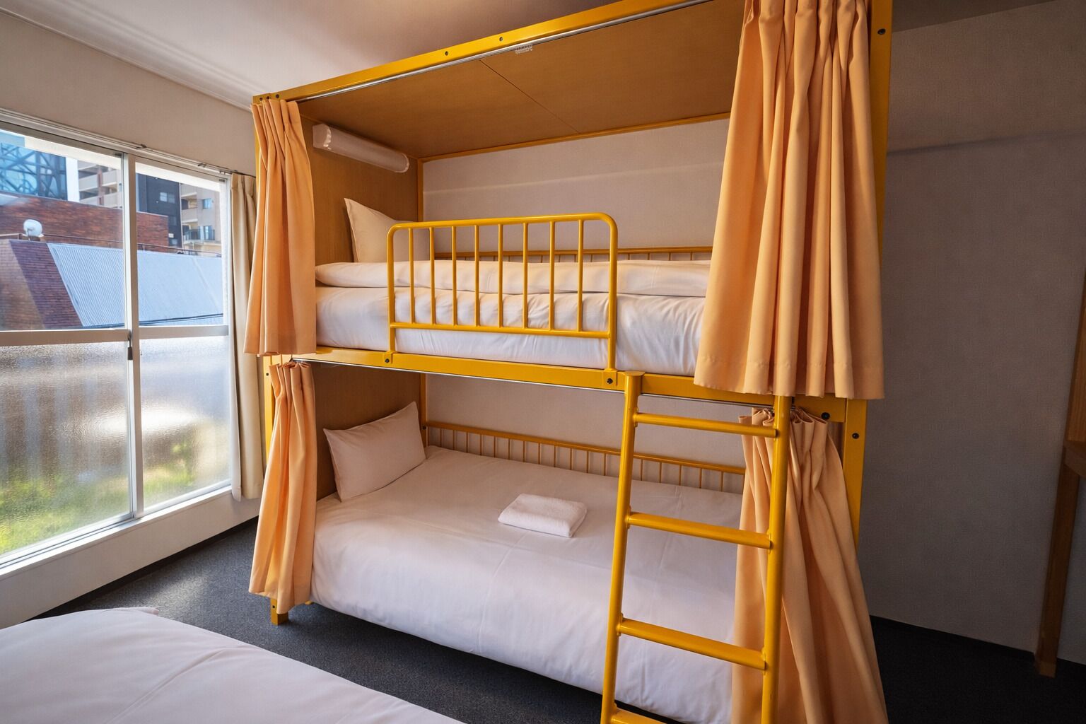 A bunk bed room with curtains, a window, and a view of buildings outside.