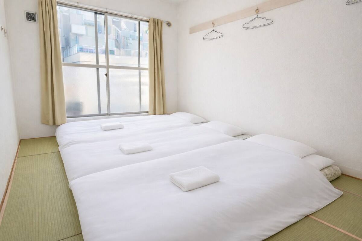 A hotel room with three beds, a window with curtains, and a view of buildings outside.