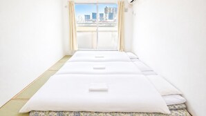 Habitación de hotel con puerta de vidrio corredera que da a un balcón, cama con colchón y almohada blancos, y unidad de aire acondicionado visible.