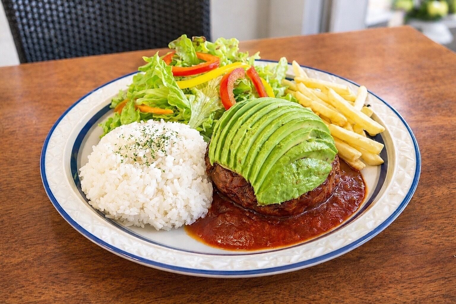 A plate with white rice, a meat patty topped with avocado slices, a side salad, and French fries.