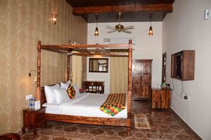 A four-poster bed with a wooden frame, a small bedside table, a nightstand, a wooden cabinet, and a television mounted on the wall. - Sadda Pind (Amritsar)