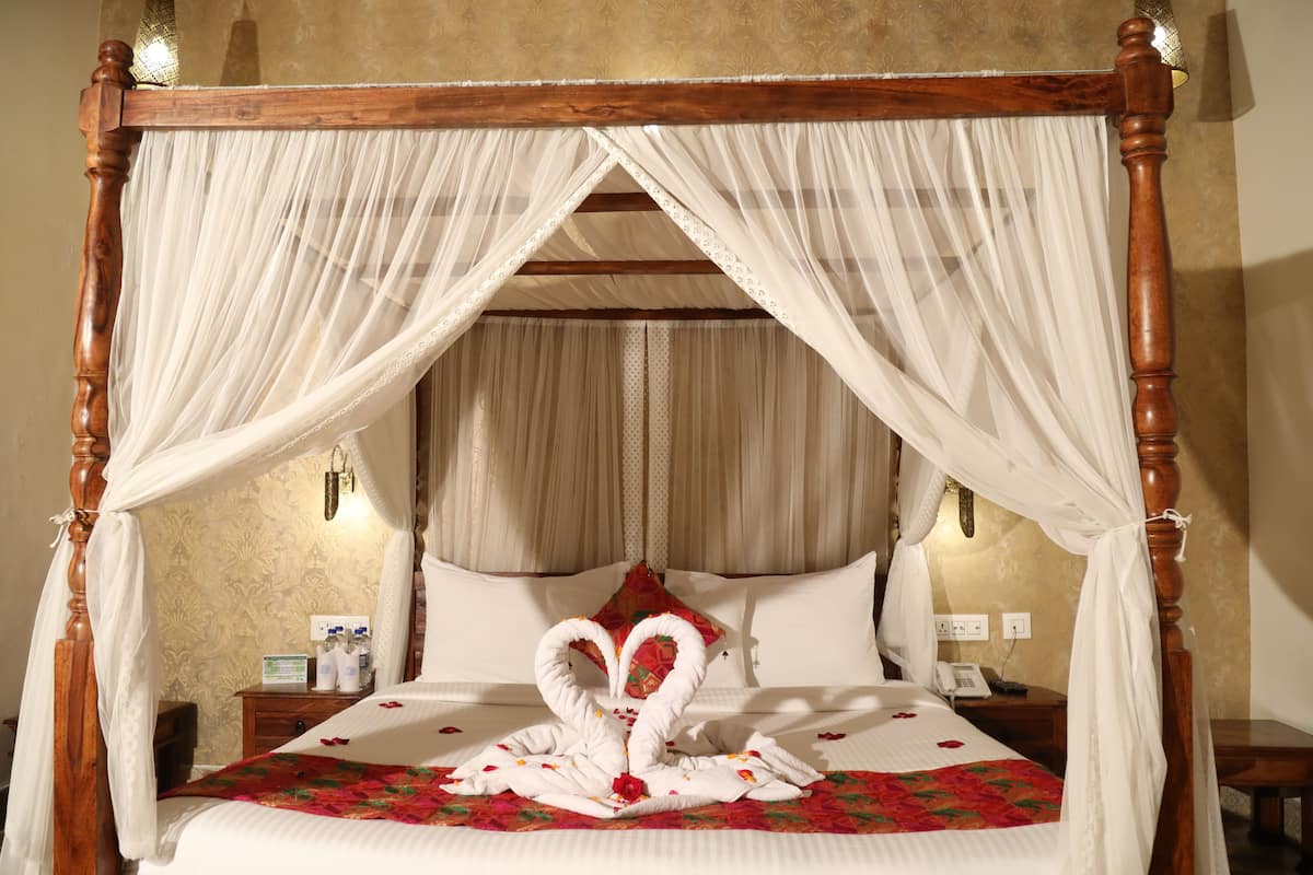 A four-poster bed with a canopy, a floral-patterned wall, and a bedside table with a lamp.