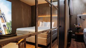 Ein Hotelzimmer mit einem Bett, einem Schreibtisch, einem Stuhl und einem Fernseher, der eine Stadtansicht zeigt.