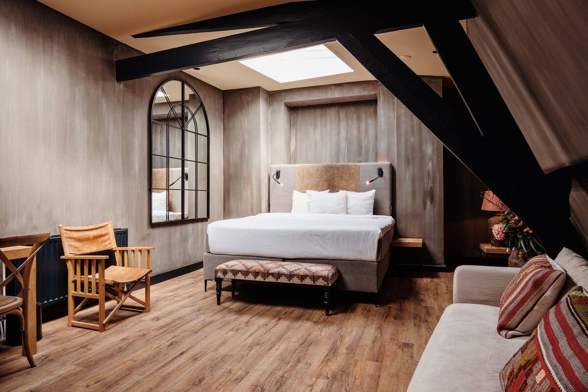 A bedroom with a large bed, a wooden chair, a bench, and a sofa.