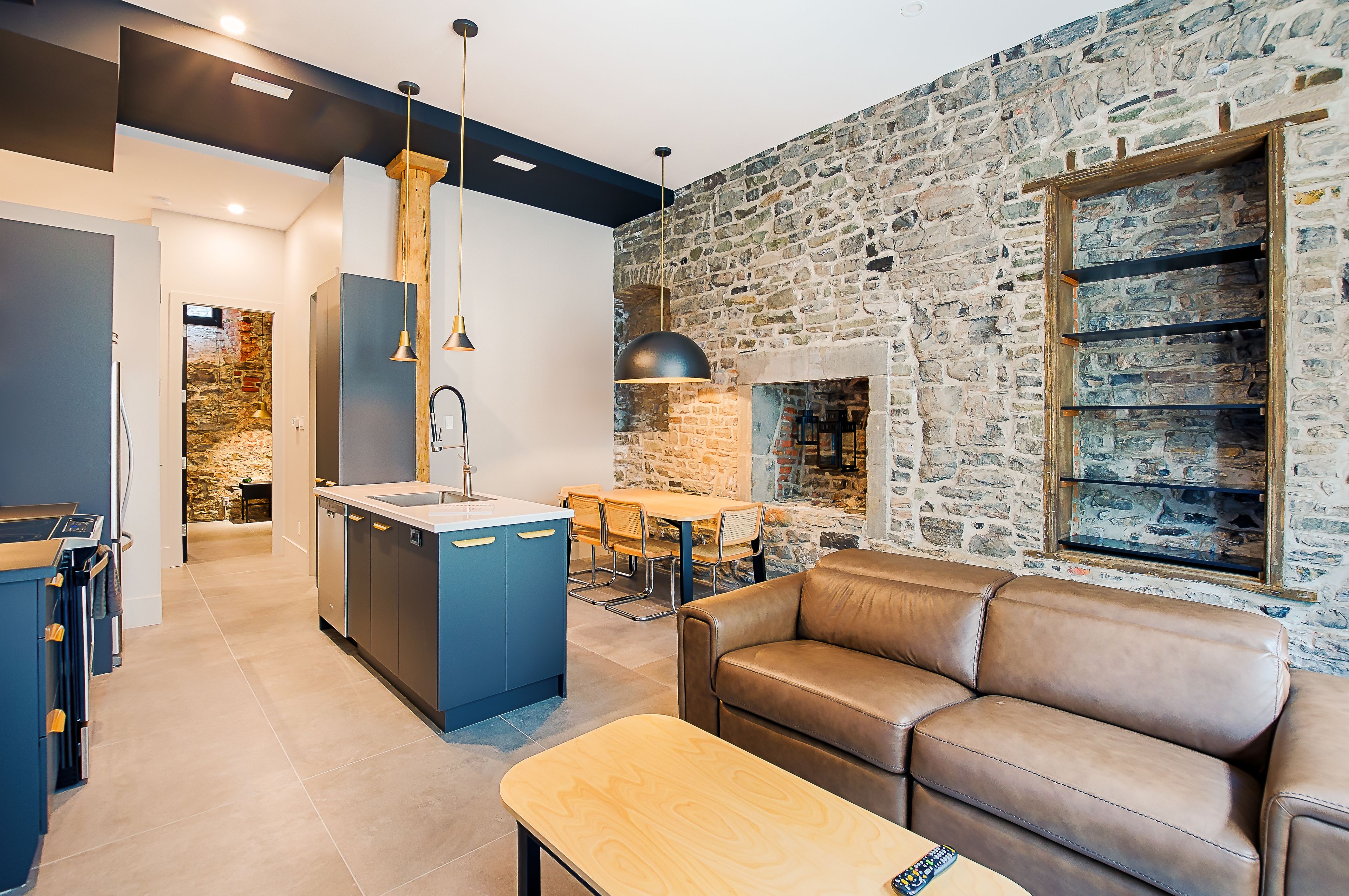 A modern kitchen with a stone wall, a dining area with a table and chairs, and a leather sofa.