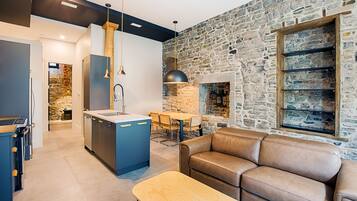 A modern kitchen with a stone wall, a dining area with a table and chairs, and a leather sofa.
