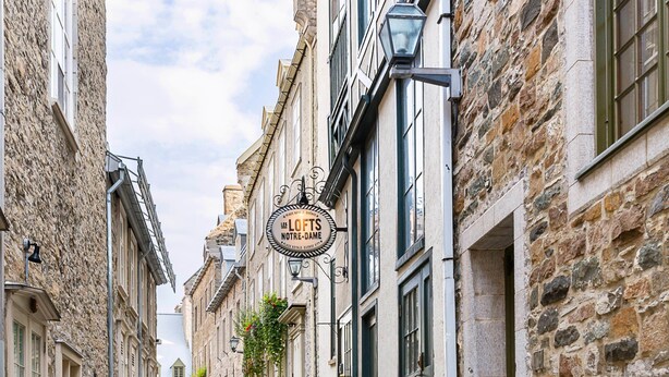 Een straat met stenen bestrating, omzoomd door historische gebouwen, waaronder een bordje met 'Le Lofts Notre-Dame'.