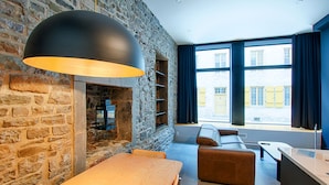 Een modern interieur met een stenen muur, een houten tafel, een leren bank en grote ramen met gordijnen.