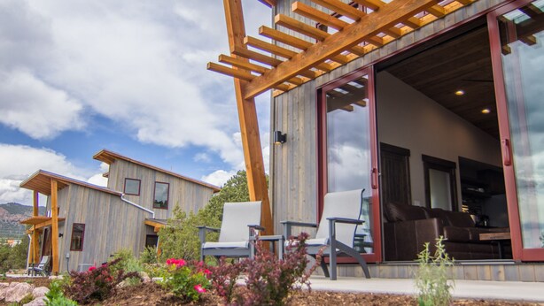 A modern house with a wooden pergola, large sliding glass doors, and a well-maintained garden with various plants and flowers. - Royal Gorge Cabins (Canon City)