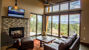 A living room with a fireplace, leather furniture, and large windows offering a mountain view. - Royal Gorge Cabins (Canon City)