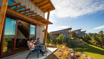 A modern house with a wooden exterior, large glass windows, and a patio area where two people are seated.