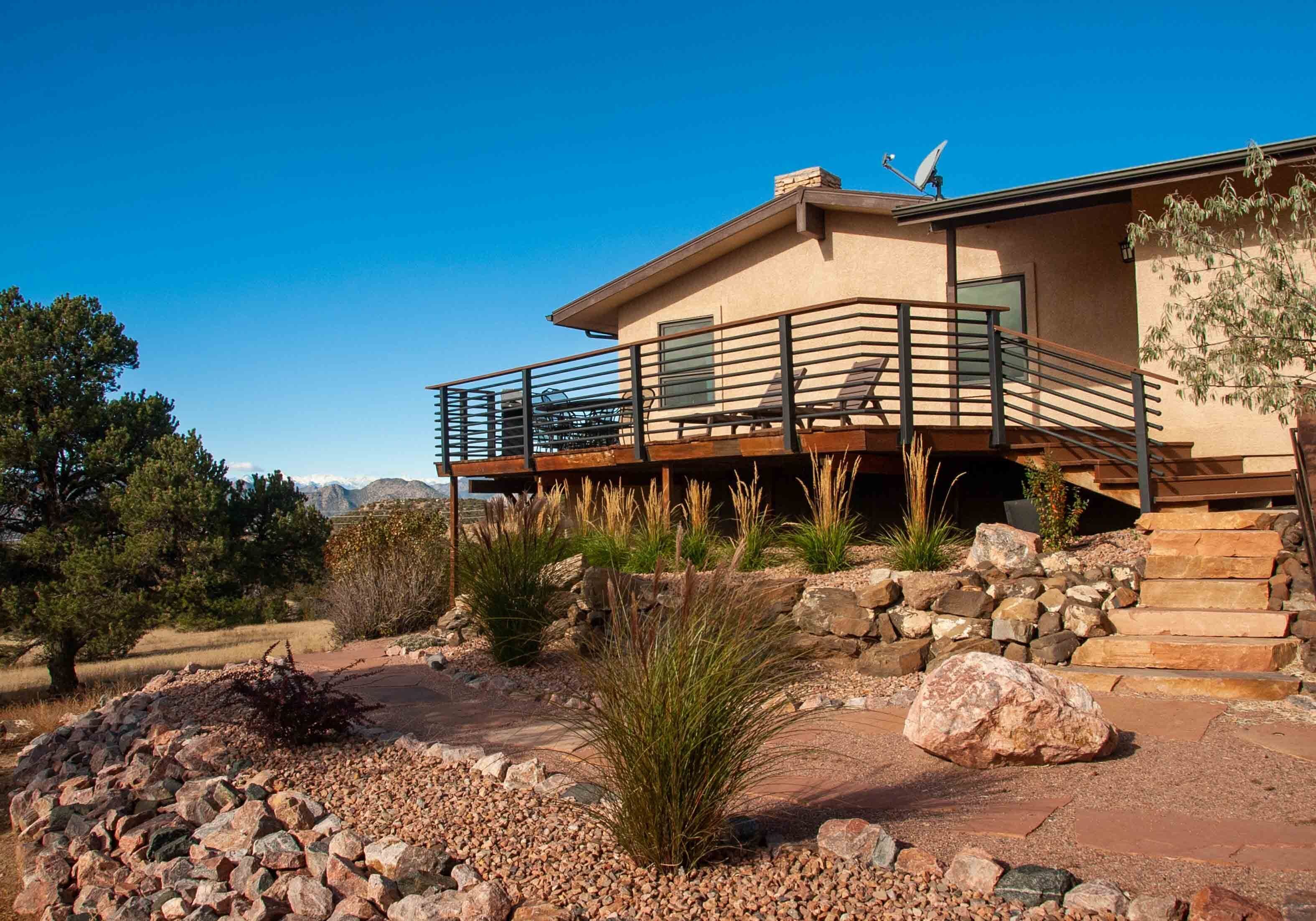 A modern house with a balcony, stone steps, and a landscaped garden.