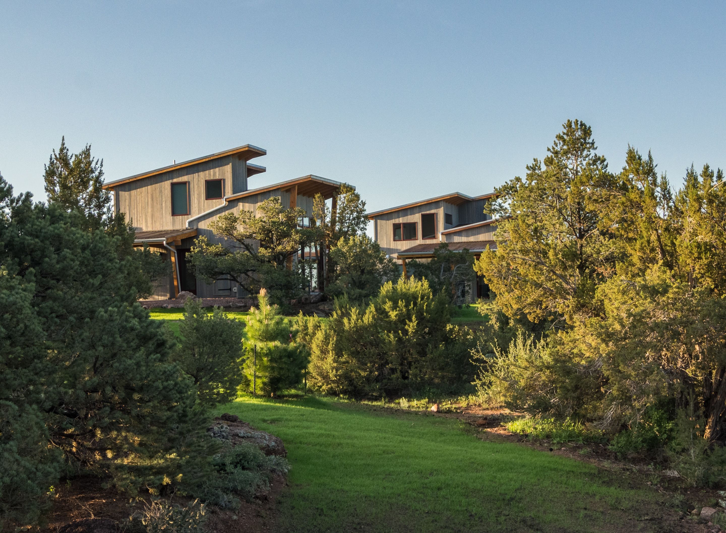 A modern two-story house with a wooden exterior, surrounded by a well-maintained garden and trees.