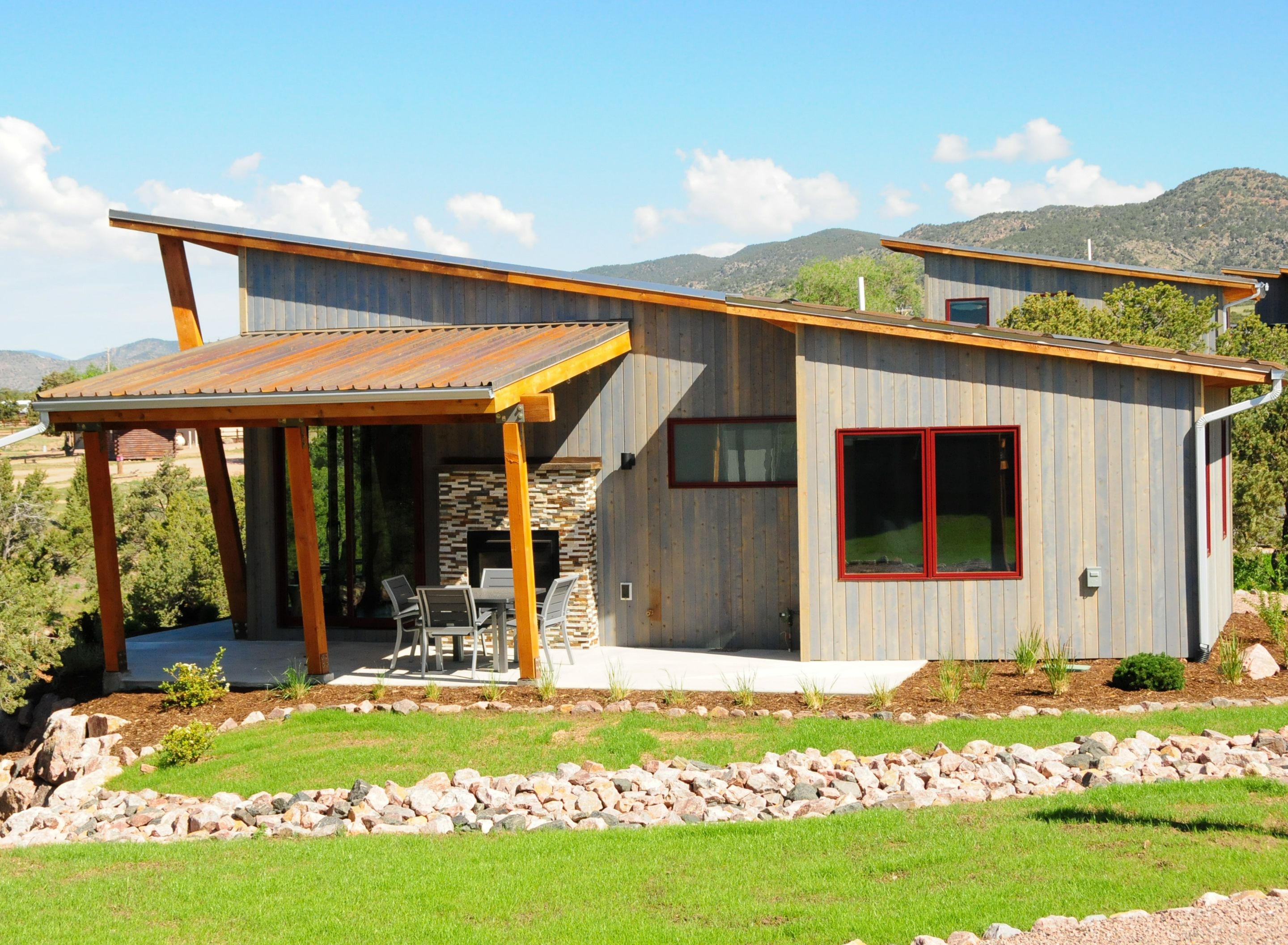 A modern house with a patio, stone fireplace, and a view of the mountains.