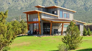 A modern two-story house with a patio area, large windows, and a view of a mountainous landscape. - Royal Gorge Cabins (Canon City)